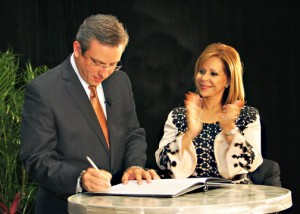 Gov. García-Padilla signs the executive order creating the council, as PRMA President Waleska Rivera looks on. 