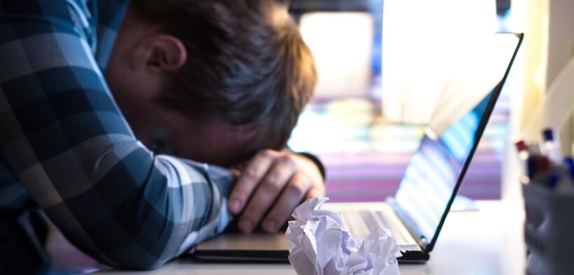 Sad and tired man in home or modern business office at night. Unemployed job seeker or businessman with ripped paper and laptop on table. No motivation or inspiration. Writer`s block or out of ideas. Artificial intelligence has made it easier for fake listings to circulate, wasting applicants’ time and eroding trust in the hiring process. (Credit: Tero Vesalainen | Dreamstime.com)