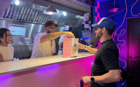 From left: Grace Martínez and Alex García-González, founder of Flatbelgel and El Colmadito de En La Madre, hand over a dish to a customer at 129 Gastropark in Arecibo, Puerto Rico, during the restaurants’ opening weekend.